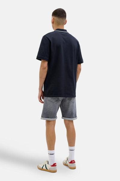 Donkerblauwe polo met korte mouwen van JACK & JONES, gedragen met een grijze spijkerbroek en sportschoenen.