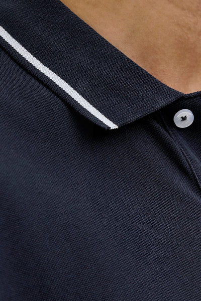 Polo bleu foncé à manches courtes de JACK & JONES, avec col à rayure blanche et bouton blanc.

