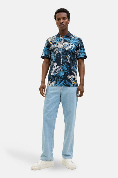 Polo bleu à manches courtes de JACK & JONES, avec motif tropical et porté avec jean clair et sneakers.