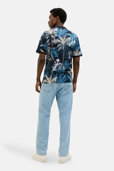 Polo bleu à manches courtes de JACK & JONES, imprimé avec des motifs de feuilles et porté avec un jean clair.