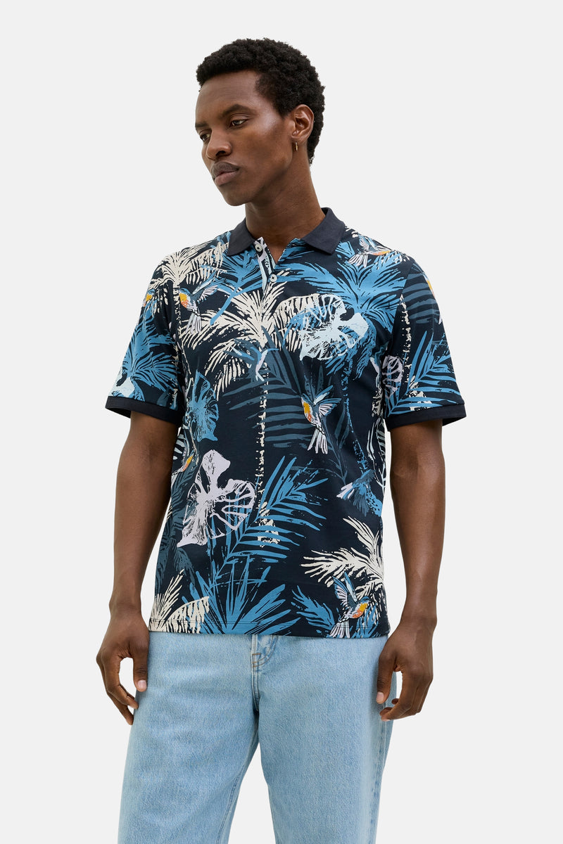 Polo bleu à manches courtes de JACK & JONES, avec imprimé tropical de palmiers et d'oiseaux, porté avec un jean clair.