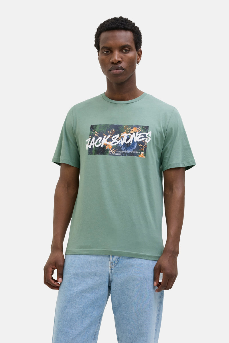 Kaki T-shirt met korte mouwen van JACK & JONES met bloemenprint en tekst op de voorkant, gedragen met een verbleekte spijkerbroek.