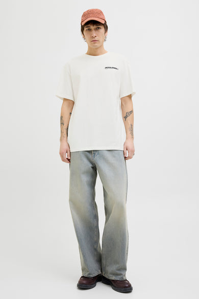 T-shirt blanc à manches courtes de Originals by Jack & Jones, porté avec un jean ample délavé et une casquette.
