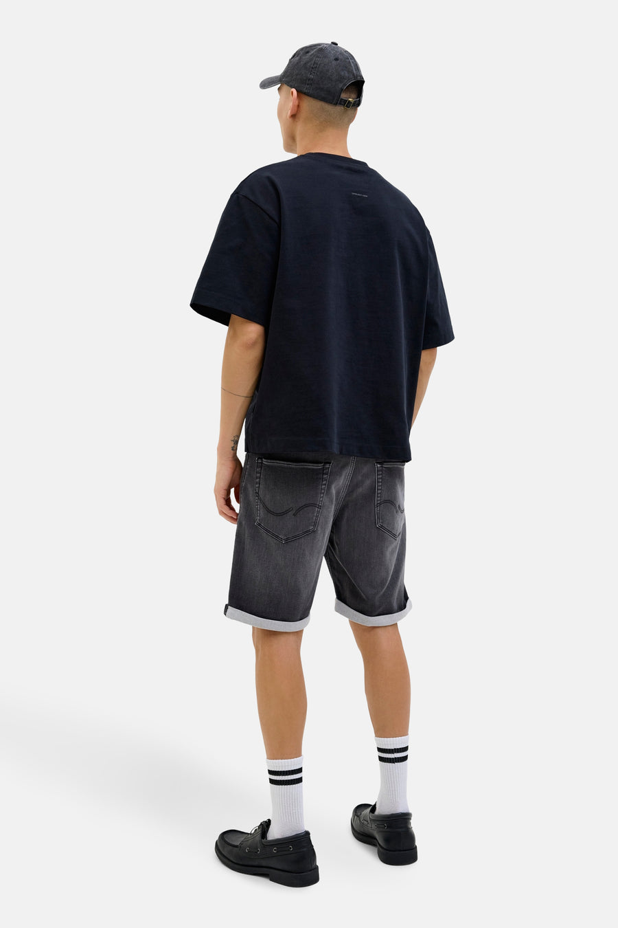 Short en denim noir de Jack & Jones, porté avec un t-shirt bleu marine, des chaussettes rayées et des mocassins noirs.