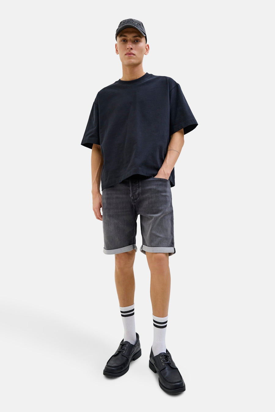 Short en jean délavé de JACK & JONES JEANS INTELLIGENCE avec ourlets retroussés, porté avec un t-shirt noir, des chaussettes blanches et des chaussures noires.