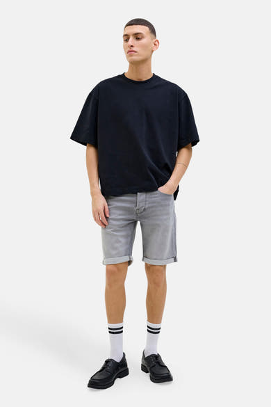Short en jean gris de JACK & JONES, porté avec un t-shirt noir oversize, des chaussettes rayées et des chaussures bateau noires.