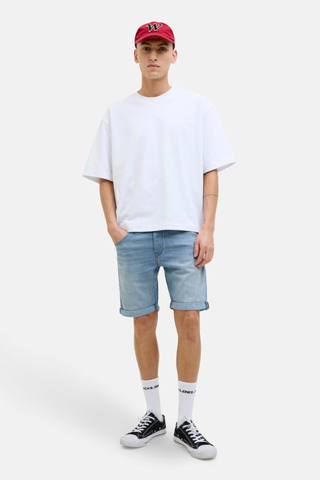Korte spijkerbroek in lichtblauw van JACK & JONES, gedragen met een wit T-shirt en een rode pet.