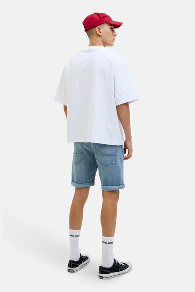 Short en denim bleu clair de JACK & JONES, avec ourlets retroussés, porté avec un t-shirt blanc et une casquette rouge.
