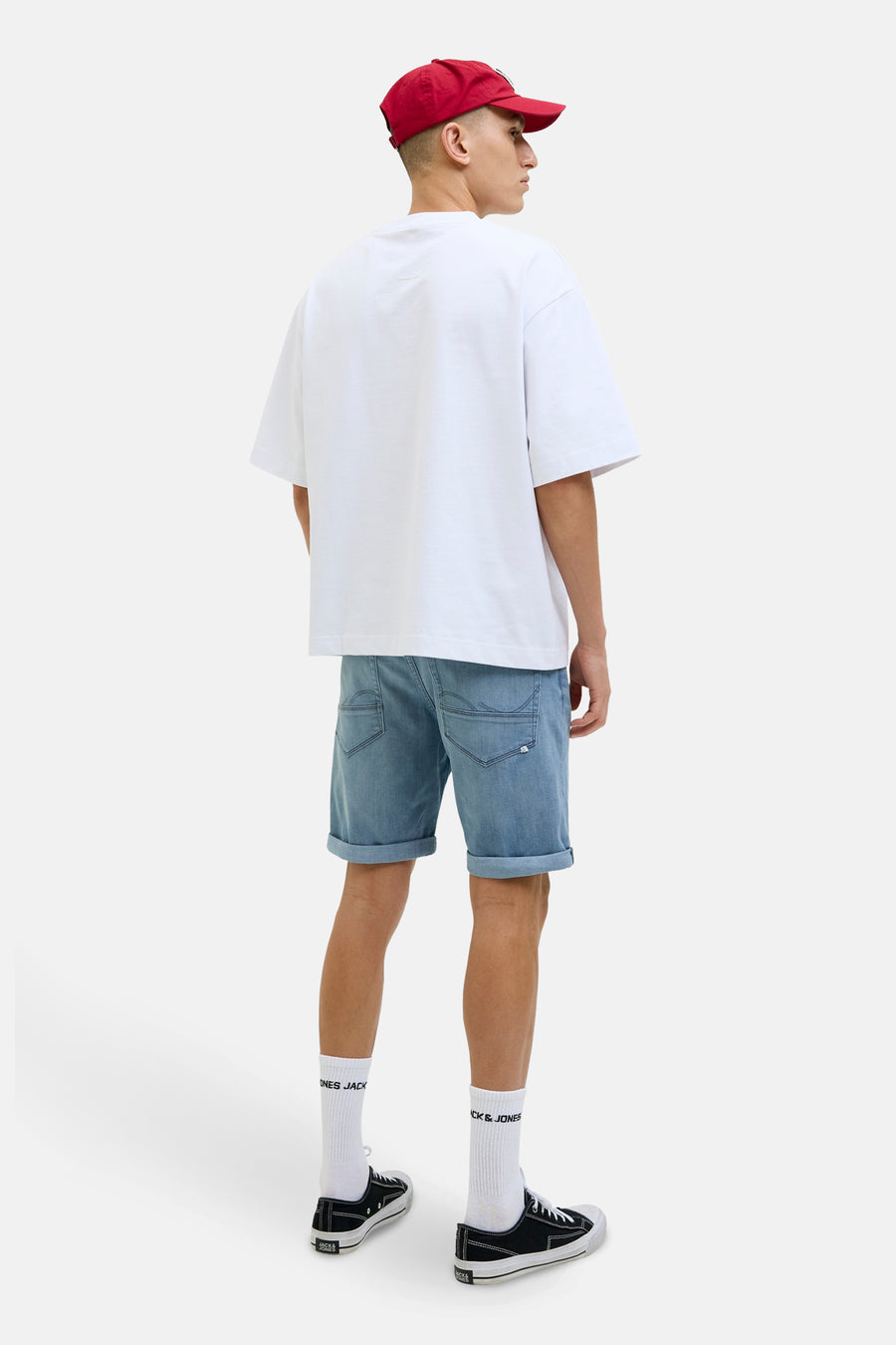 Short en denim bleu clair de JACK & JONES, avec ourlets retroussés, porté avec un t-shirt blanc et une casquette rouge.

