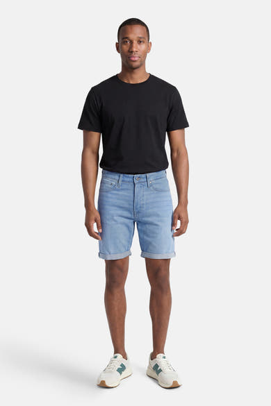 Short en jean bleu clair de JACK & JONES, porté par un homme avec un t-shirt noir et des baskets blanches, ourlet retroussé.
