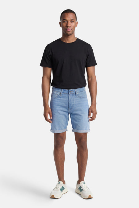 Lichtblauwe spijkerbroek van JACK & JONES, gedragen door een man met een zwart T-shirt en witte sneakers, opgerolde zoom.