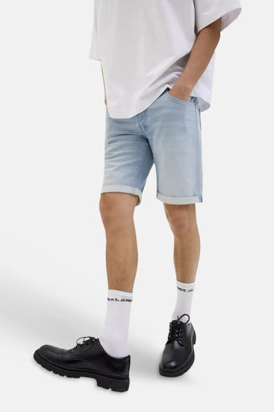Short en jeans bleu de JACK & JONES à l'ourlet retroussé, porté avec un t-shirt blanc, des chaussettes et des chaussures noires.