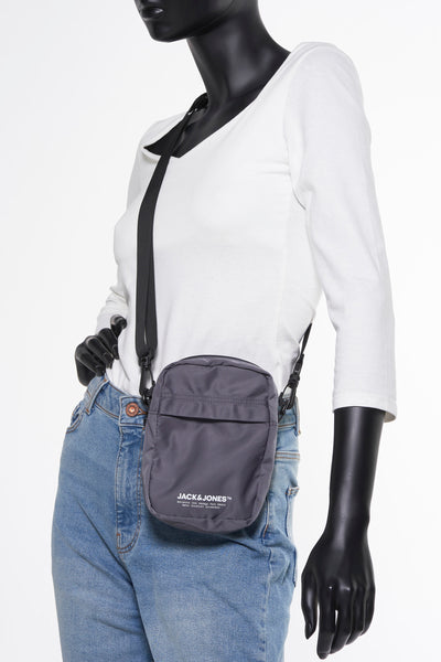 Grijze schoudertas van ACCESSORIES BY JACK & JONES, gedragen met een wit T-shirt en een lichtblauwe jeans.
