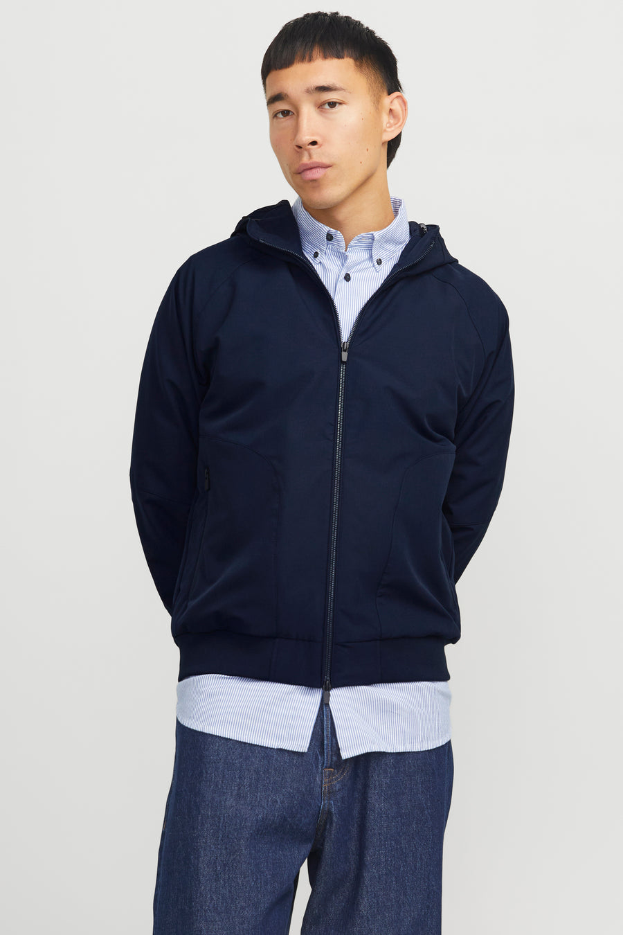 Donkerblauwe regenjas van JACK & JONES, gedragen over een gestreept overhemd en een blauwe spijkerbroek.