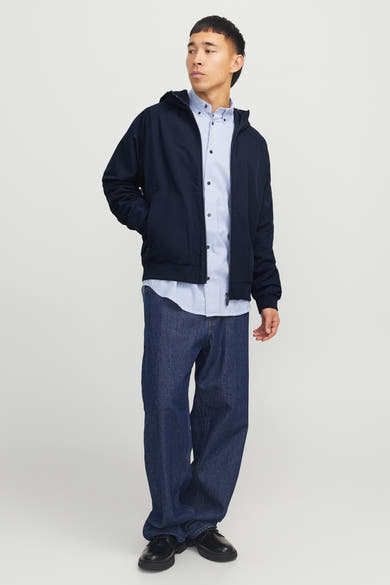 Donkerblauwe regenjas van JACK & JONES, gedragen met een gestreept overhemd en een wijde jeans.