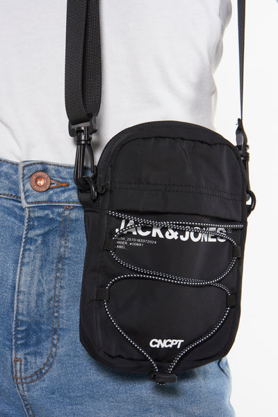 Zwarte schoudertas van ACCESSORIES BY JACK & JONES met decoratieve koorden, gedragen met een blauwe jeans en een wit T-shirt.