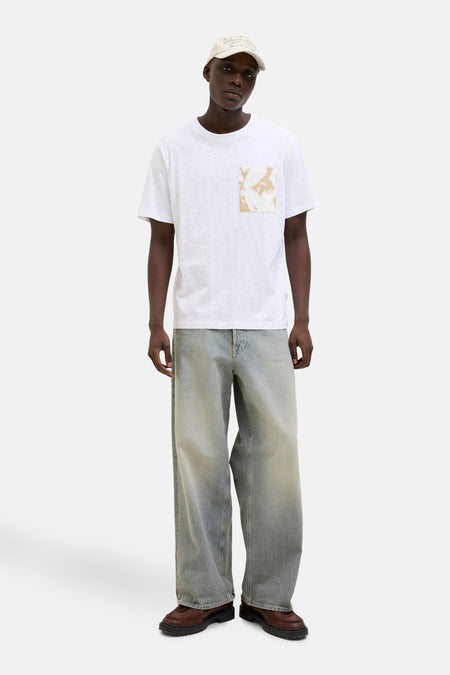 Wit T-shirt met korte mouwen van ORIGINALS BY JACK & JONES met abstracte opgedrukte zak, gedragen met een spijkerbroek en een pet.