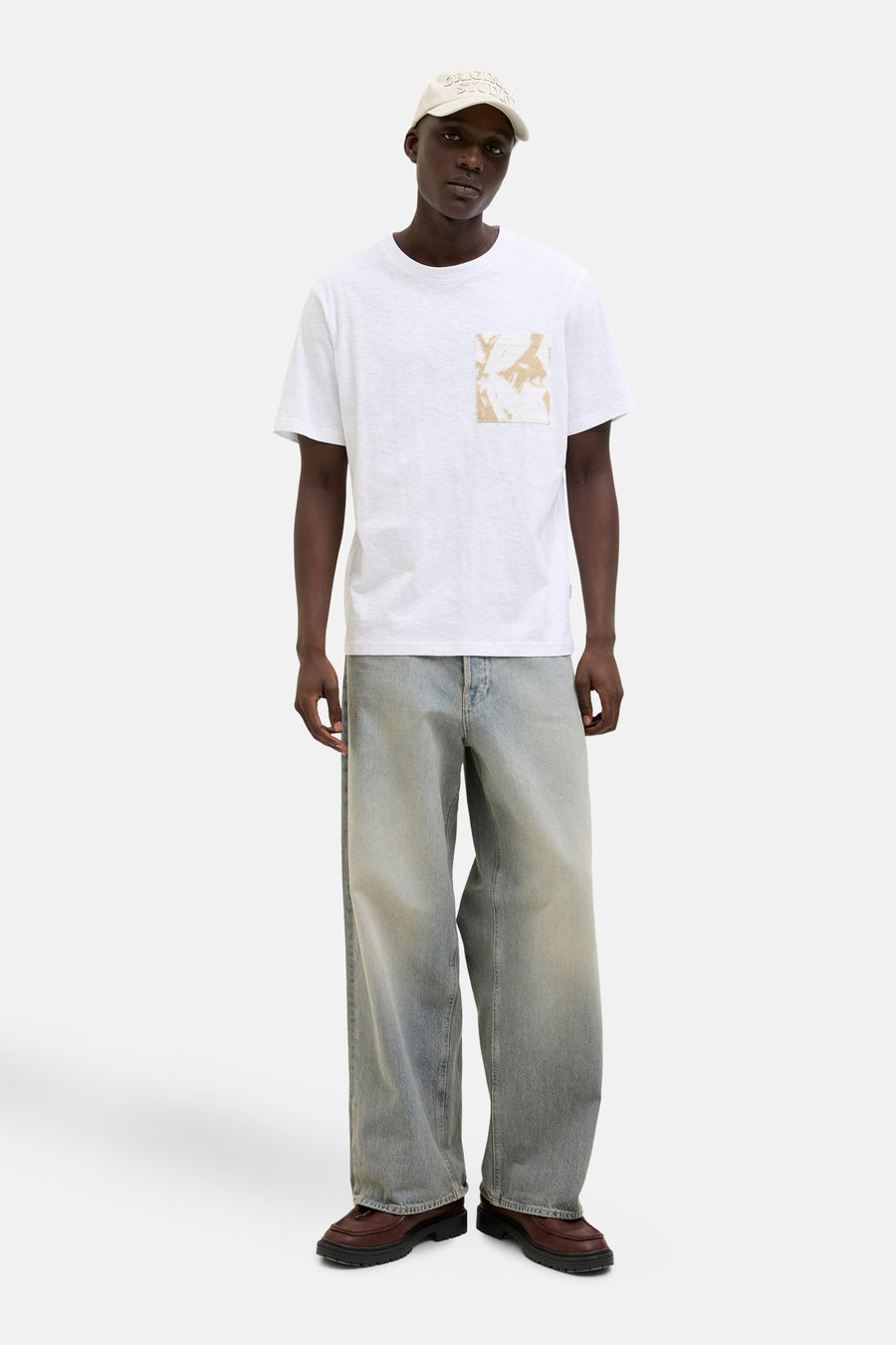 Wit T-shirt met korte mouwen van ORIGINALS BY JACK & JONES met abstracte opgedrukte zak, gedragen met een spijkerbroek en een pet.