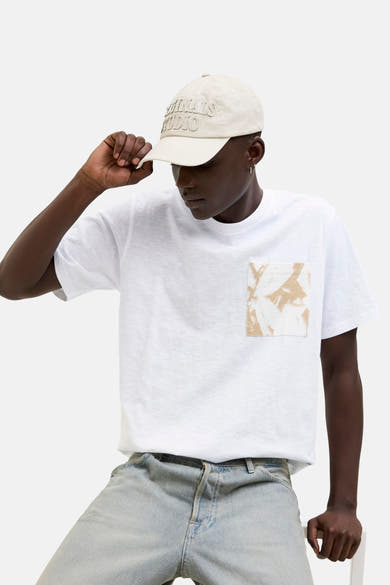 Wit T-shirt met korte mouwen van ORIGINALS BY JACK & JONES, met een bedrukte zak, gedragen met een hoed en een spijkerbroek.