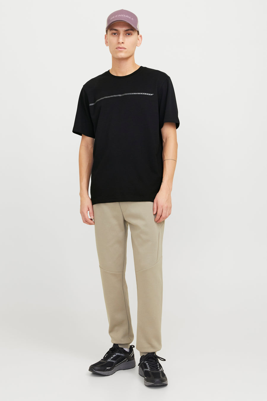 Zwart T-shirt met korte mouwen van JACK & JONES, met een horizontale streep op de borst, gedragen met een beige broek en zwarte sneakers.