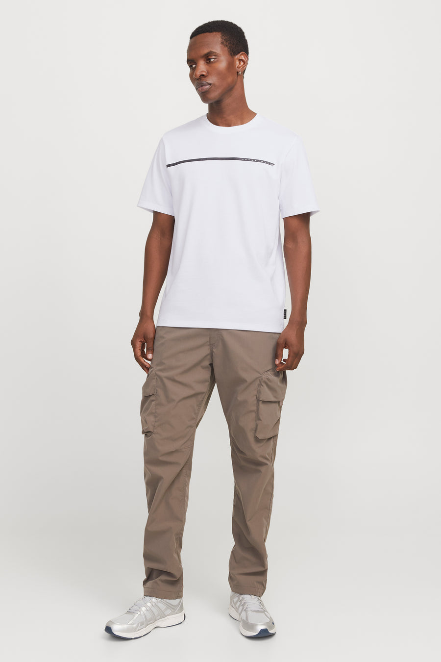 Wit T-shirt met korte mouwen van JACK & JONES, met horizontale streep op de voorkant, gedragen met een bruine cargobroek en zilveren sneakers.