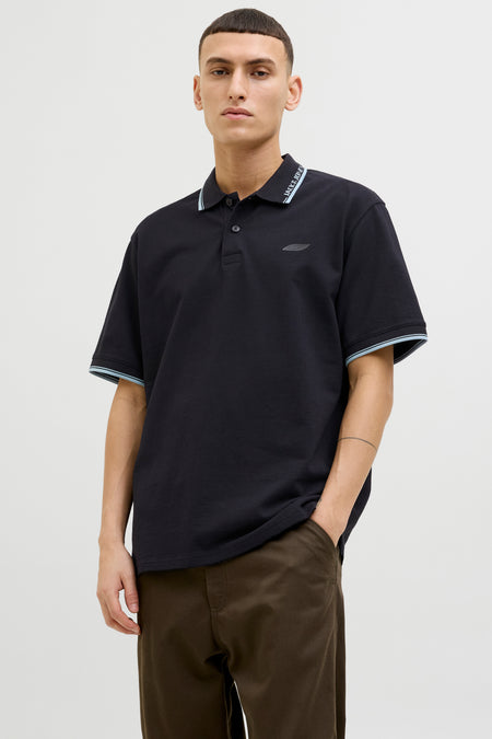 Zwart poloshirt met korte mouwen van JACK & JONES, met gestreepte bies op de kraag en mouwen, gedragen met een bruine broek.