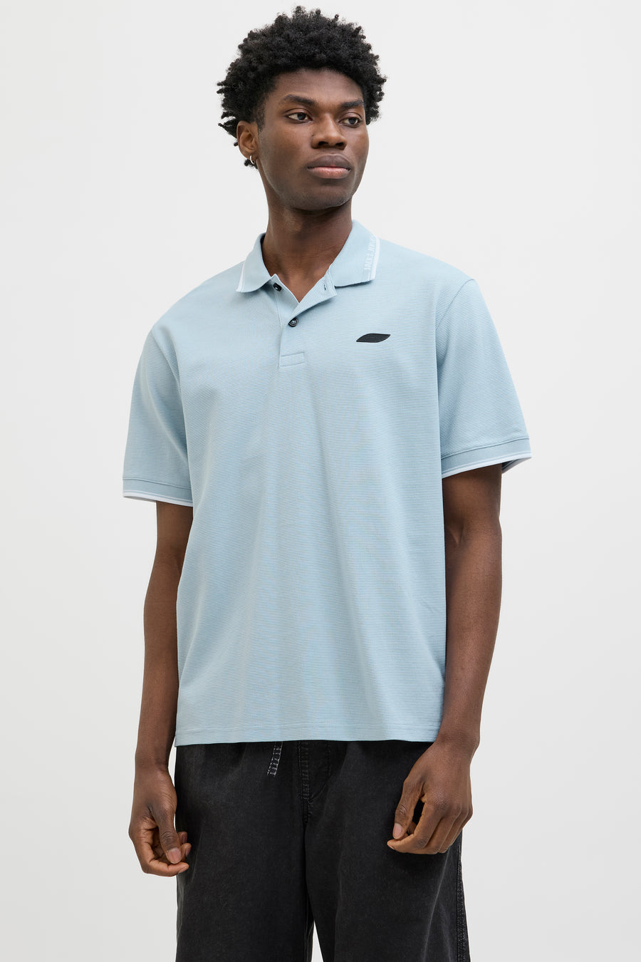 Blauw poloshirt met korte mouwen van JACK & JONES, gedragen met een wijde zwarte broek en zilveren sneakers.