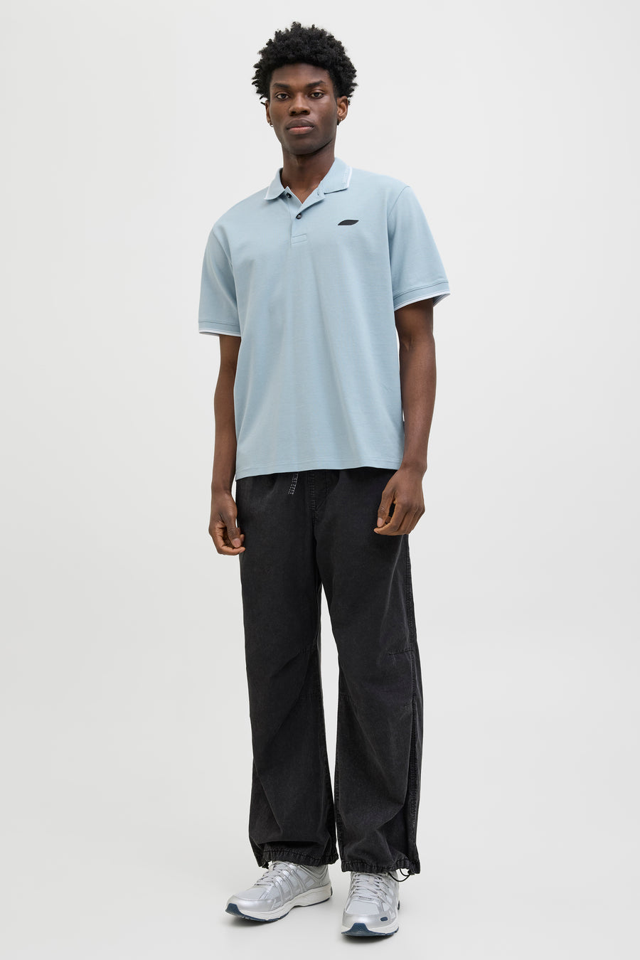 Polo bleu à manches courtes de JACK & JONES, porté avec un pantalon noir ample et des baskets argentées.