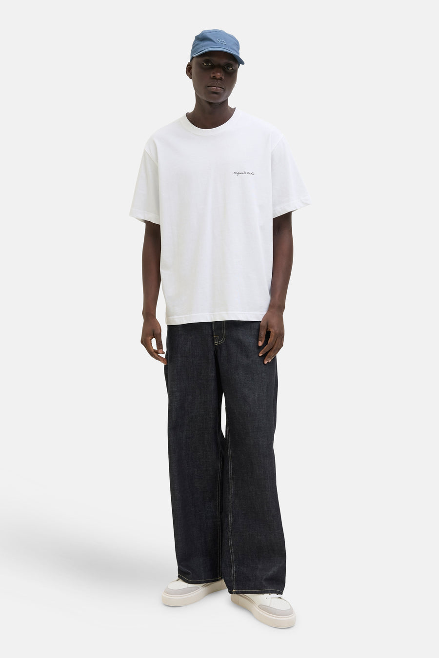 T-shirt blanc à manches courtes par ORIGINALS BY JACK & JONES, porté avec un pantalon denim ample et une casquette.
