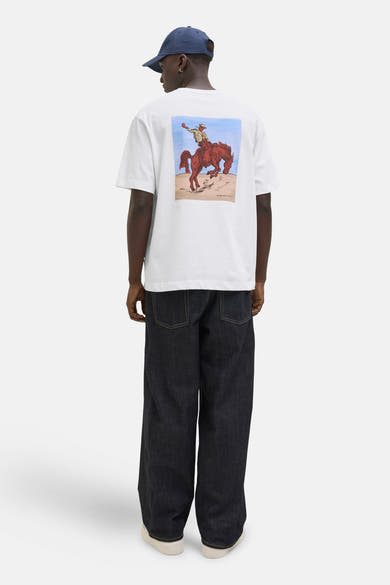 Wit T-shirt met korte mouwen van ORIGINALS BY JACK & JONES met een print van een cowboy op een paard, gedragen met een wijde donkerblauwe jeans.