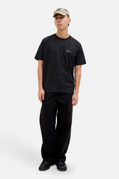 T-shirt noir à manches courtes par ORIGINALS BY JACK & JONES, porté avec un pantalon noir ample et une casquette beige.
