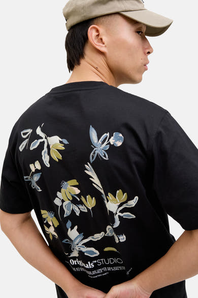 Zwart T-shirt met korte mouwen van ORIGINALS BY JACK & JONES met bloemenprint op de rug, gedragen met een beige pet.