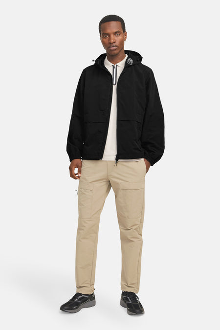 Korte zwarte jas van JACK & JONES, met capuchon en cargozakken, gedragen met een lichtgekleurd poloshirt en een beige broek.