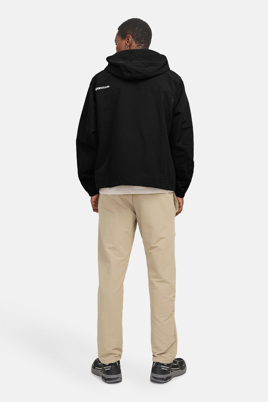Korte zwarte jas van JACK & JONES, met capuchon en subtiele print op de rug, gedragen met een beige broek.
