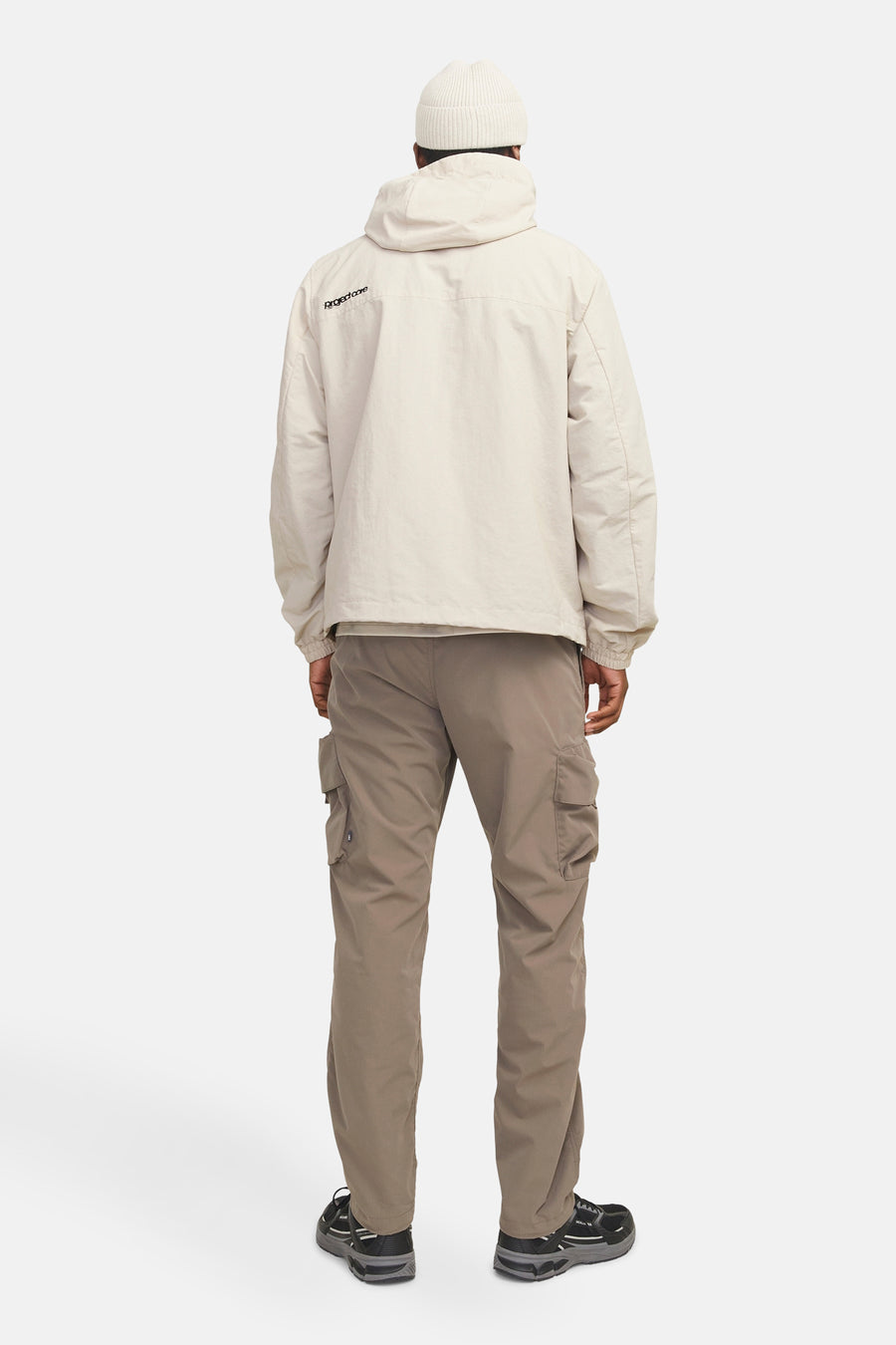 Korte beige jas JACK & JONES met capuchon, achteraanzicht en bruine cargobroek gedragen.
