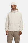 Korte beige jas van JACK & JONES, met capuchon en ritssluiting, gedragen met een crèmekleurige muts en een cargobroek.