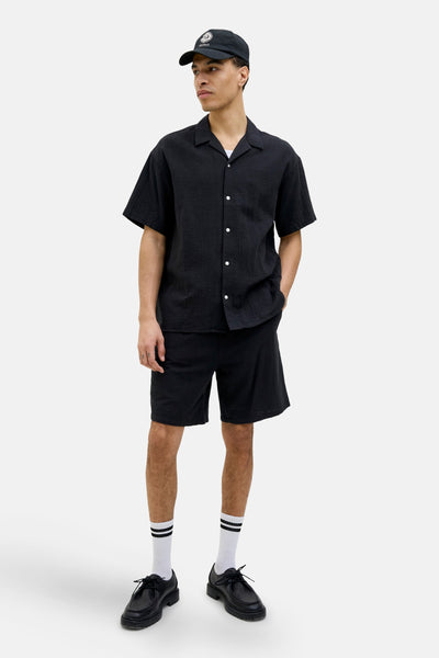 Korte noir van ORIGINALS BY JACK & JONES, gedragen met een zwart overhemd met korte mouwen en gestreepte sokken.