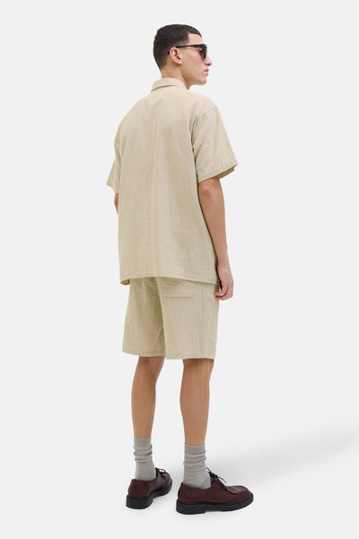 Beige overhemd met korte mouwen van ORIGINALS BY JACK & JONES, gedragen met een bijpassende korte broek, grijze sokken en bruine schoenen.