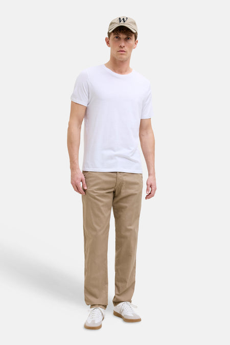 Pantalon coloré beige de JACK & JONES, porté avec un t-shirt blanc et une casquette.