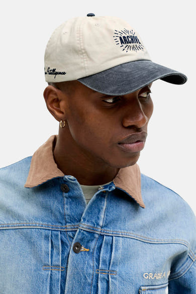 Beige pet met een marineblauwe klep en borduursel aan de voorkant, van Accessories by Jack & Jones, gedragen met een blauwe spijkerjas.