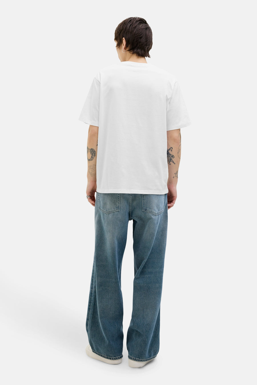 Wit T-shirt met korte mouwen van Originals by Jack & Jones, gedragen met een wijde jeans en tatoeages.