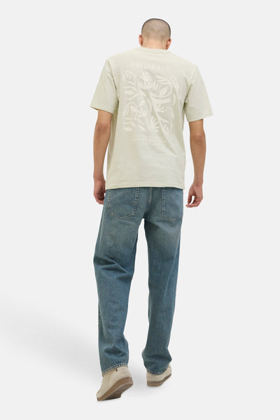 Groen T-shirt met korte mouwen van JACK & JONES, met een gestileerd bloemenpatroon op de rug, gedragen met een blauwe jeans en crèmekleurige schoenen.