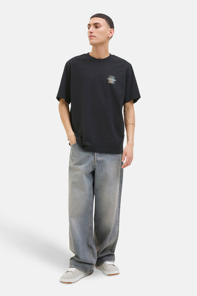 T-shirt à manches courtes noir de JACK & JONES, avec un motif carré sur la poitrine, porté avec un jean ample.
