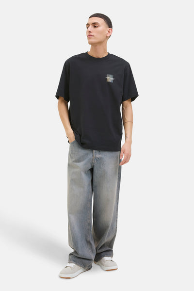 T-shirt à manches courtes noir de JACK & JONES, avec un motif carré sur la poitrine, porté avec un jean ample.
