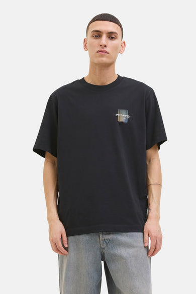 T-shirt noir à manches courtes de JACK & JONES, avec un logo graphique sur la poitrine, porté avec un jean délavé.
