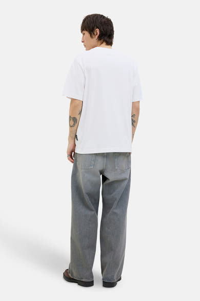 T-shirt à manches courtes blanc de JACK & JONES, porté avec un jean ample et des chaussures marron.