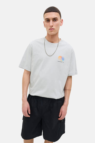 Grijze T-shirt met korte mouwen van JACK & JONES, gedragen met een zilveren ketting en een zwarte korte broek.