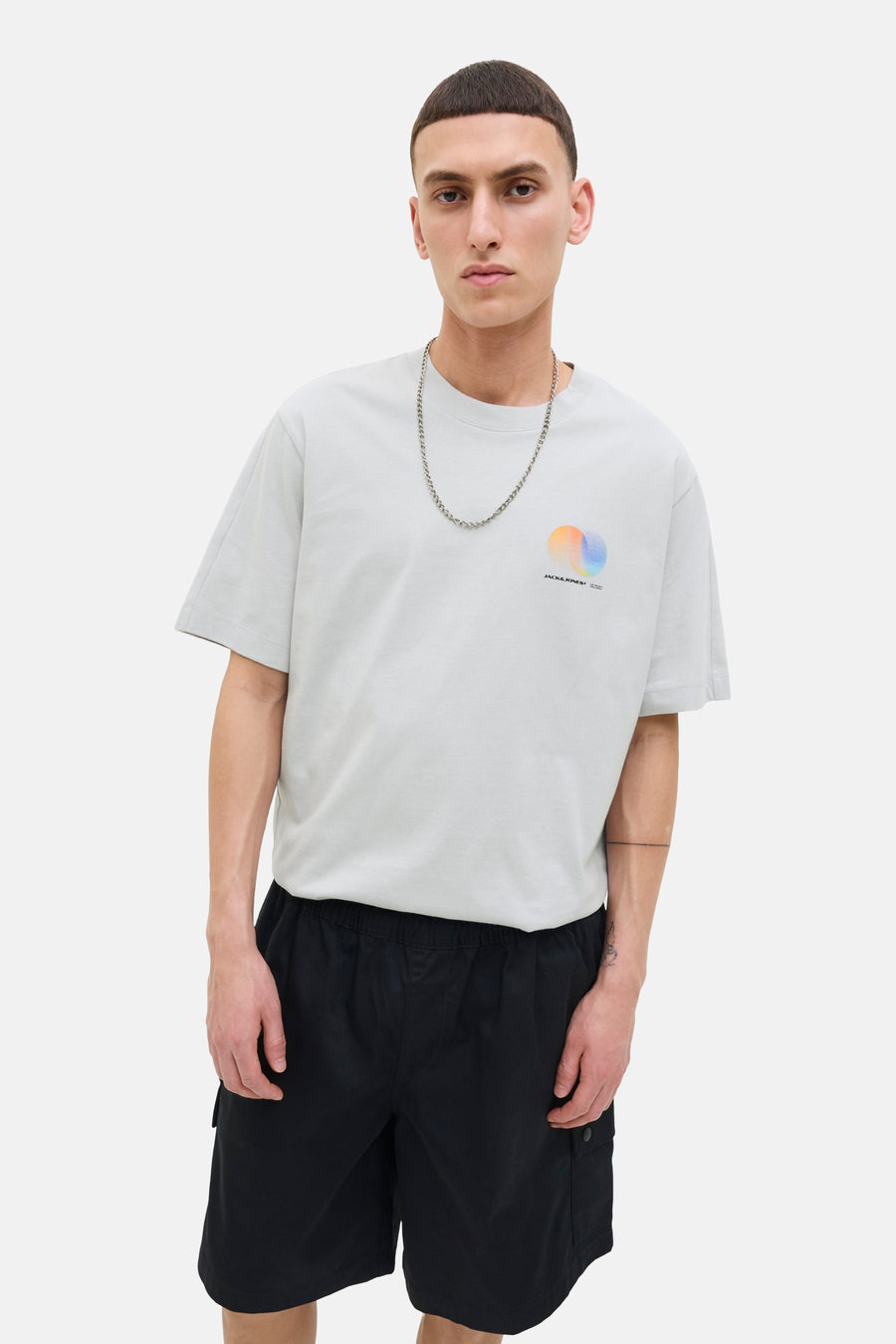 Grijze T-shirt met korte mouwen van JACK & JONES, gedragen met een zilveren ketting en een zwarte korte broek.