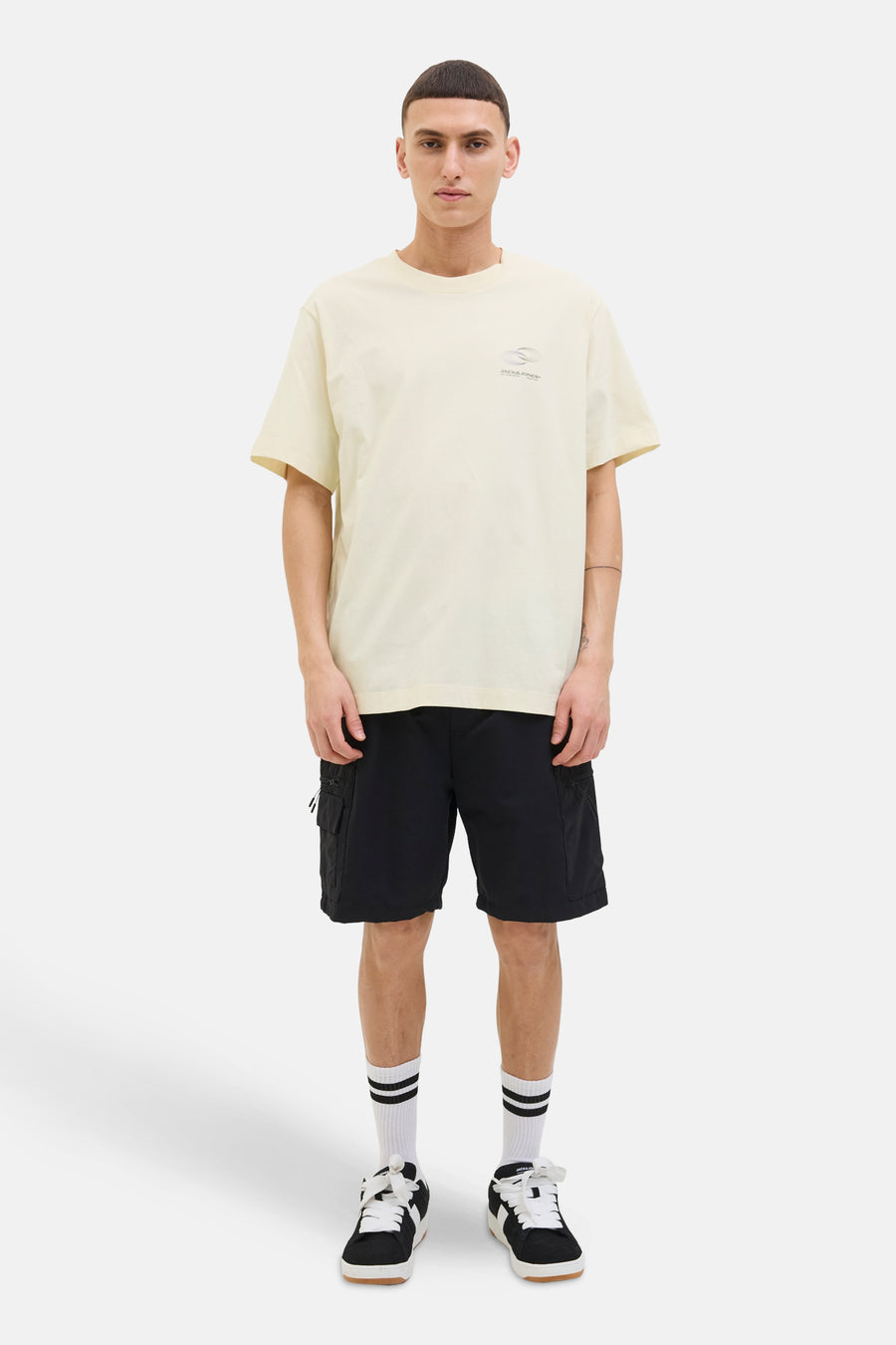 Beige T-shirt met korte mouwen van JACK & JONES, gedragen met een zwarte korte broek en sportschoenen.