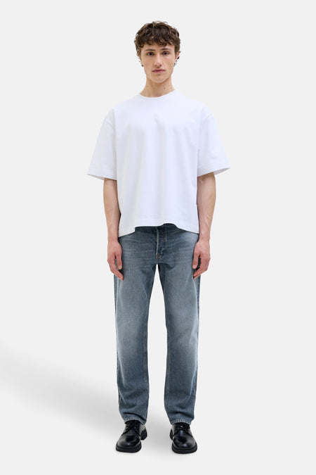 Taps toelopende jeans in middinblauw denim van JACK & JONES JEANS INTELLIGENCE, gedragen met een wit T-shirt en zwarte schoenen.
